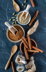A top down view of a selection of complimentary Indian spices including cinnamon, ginger and cardamom in both ground powder form and whole form.
