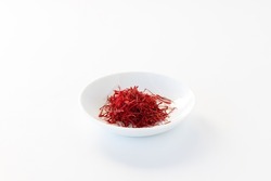 Close up of a small dish filled with Saffron threads against a white background.