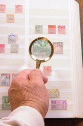 Maginfying glass held in a hand to  view stamp in a philatelic collection
