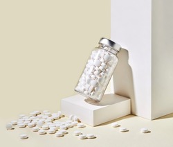 White tablets in a glass jar on the pastel yellow background. Medication in tablets. Copy space