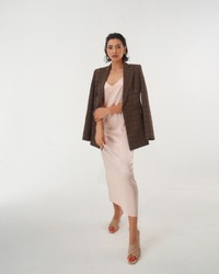 Elegant woman in peach color silk slip dress and brown squared wool blazer standing and posing in studio at white background. Pretty stylish brunete girl with makeup and wet hair full length portrait