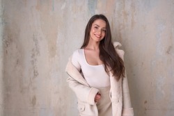Young stylish caucasian brunette woman posing in white sheepskin coat against wall