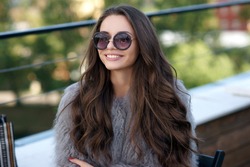 Trendy dressed fashionable girl wearing fur coat. Young pretty beautiful woman with long curly hair looking at you.