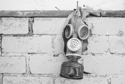 Old gas mask with coal filter hung on the brick wall. Black and white. Concept - Nuclear Disarmament and Radiation Protection, epidemic, coronavirus, covid-19, pandemic.