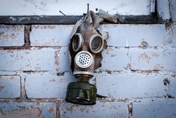 Old gas mask with coal filter hung on the brick wall. Concept - Nuclear Disarmament and Radiation Protection, epidemic, coronavirus, covid-19, pandemic.