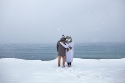 A couple in love walks on the shore of the winter sea, a man and a woman are frozen, it is snowing