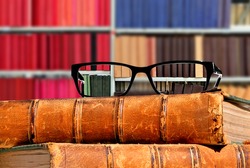 Old books and eye glasses with sharp vision through them on the books against the indistinct (unsharp, not in focus) background - Concept of visual acuity return 