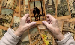 Old female hands hold old travel photo. Vintage photo cards on the wood background. Remembering Paris. European tourism and vacation travel. Memory and dreams concept.