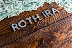words ROTH IRA laid on wooden surface by metal letters with us dollar banknotes