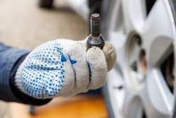 mechanic hand in fabric glove holding car wheel bolt, closeup with selective focus