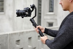 filmmaking, hobby and creativity concept - close up of professional male videographer shooting video using modern dslr camera on 3-axis gimbal over concrete building