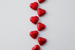 Love and Valentine's day background - close up of heart shape chocolate candies in red foil over white table background with copy space