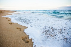 close up of footprints on sandy beach and sea wave