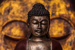The symbol of the richness, of the founder of Buddhism, Buddha miniature statue sculpture with golden painted wood carved Buddha face on the background, vivid colors