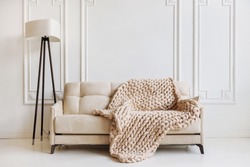Hand knitted merino wool chunky blanket in interior on background. Stylish and cozy Scandinavian interior: bed, chair, white wall.