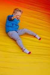 Happy little boy sliding down an a yellow- orange inflatable slide.