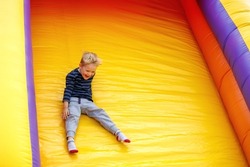 Laughing, lot of fun little boy child sliding on an inflatable multi-colored slide. Bright yellow background, free space for text.