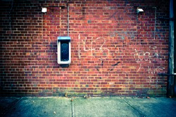 Grungy urban background of a brick wall with an old out of service payphone on it