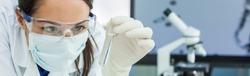 Panoramic web banner female medical or research scientist or doctor using looking at a test tube of clear solution in a lab or laboratory. Header panorama.
