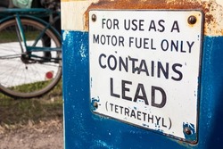 Old fashioned petrol, gas or gasoline fuel pump with lead and Tetraethyl warning sign and a bicycle in the background