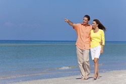 Happy man and woman couple walking and pointing on a deserted beach with bright clear blue sky