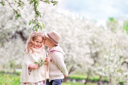 Adorable happy kids outdoors on spring day in beautiful blooming garden, little boy kissing a girl