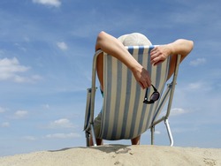 Woman sunbathing on deckchair on the beach shot against blue sky
