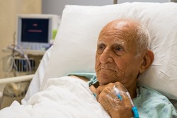 Elderly 80 plus year old man recovering from surgery in a hospital bed.