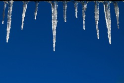 Frozen icicles hanging from a roof isolated against a blue sky background