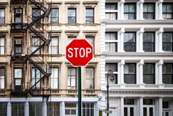 Stop sign in front of historic old buildings with windows and fire escape at the intersection of Howard and Mercer Streets in Lower Manhattan, New York City NYC