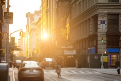 Delivery man rides bike down the streets of New York City with the sunshine reflecting off the downtown building windows