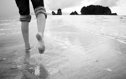 A young woman walks alone on a beach in black and white