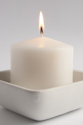 Large white candle in a square tray close up