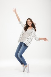 Full length image of Happy brunette woman in shirt having fun and looking at the camera over gray background