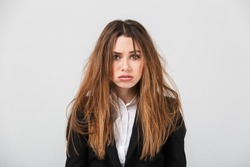 Portrait of an exhausted businesswoman dressed in suit with messy hair looking at camera isolated over gray background