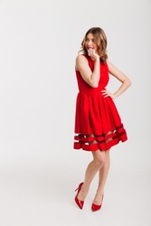 Full length portrait of a lovely petty girl dressed in red dress posing while standing and looking away at copy space isolated over white background
