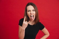 Portrait of a crazy girl showing horns up gesture isolated over pink background