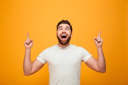 Portrait of a happy bearded man pointing fingers up at copyspace isolated over yellow background