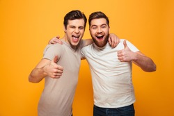 Portrait of a two happy young men showing thumbs up isolated over yellow background