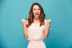 Image of excited young lady standing isolated over blue background make winner gesture.