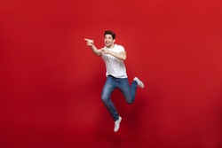 Full length portrait of a cheerful young man in white t-shirt pointing fingers away while celebrating success isolated over red background