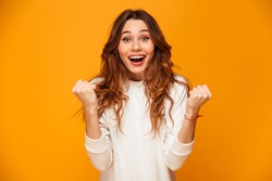 Surprised happy brunette woman in sweater rejoices and looking at the camera over yellow background