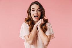 Portrait of an excited young girl in dress looking at camera isolated over pink background