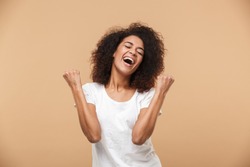 Portrait of a happy young african woman celebrating success isolated over beige background