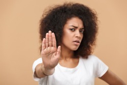 Close up portrait of a serious young african woman showing stop gesture with her palm isolated over beige background