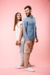 Full length portrait of a happy young couple standing back to back isolated over pink background