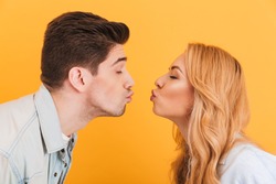Profile photo of young beautiful people in love expressing love and affection while kissing each other with closed eyes isolated over yellow background