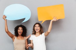 Portrait of two happy young women holding empty speech bubbles isolated over gray background