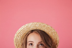 Close up half face portrait of a happy young woman in straw hat looking up isolated over pink background
