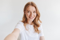 Image of young happy redhead woman isolated over white wall background make selfie looking camera.